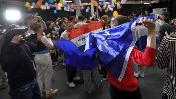 Menschen tanzen mit EU-Flagge im Medienzentrum während des zweiten Halbfinales des ESC. © picture alliance / PIXSELL Foto: Sanjin Strukic