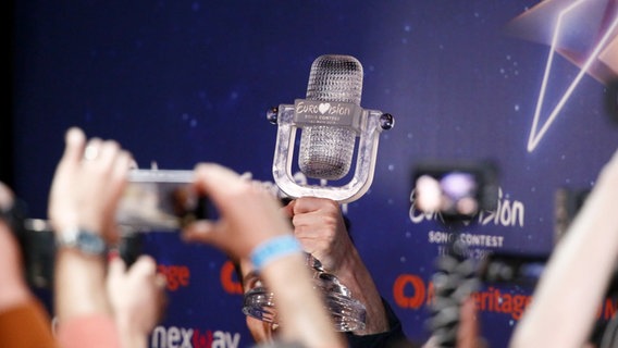 Ein Hand hält die ESC-Trophäe 2019 in die Luft, andere Händen halten Smartphones in die Luft. © eurovision.tv Foto: Andres Putting